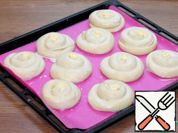 Spread the buns-pies on a covered baking sheet and grease with liquid sour cream. In the middle of the bun, put a small piece of butter (20 g). We send the buns to a warm place to rise 2 times.