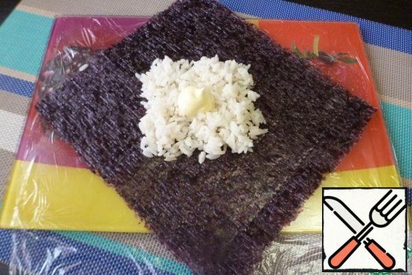 Cover the work surface with cling film. Put a rhombus leaf of nori on it. Put the rice in the middle of the squares. On top of the rice, to grease with mayonnaise.