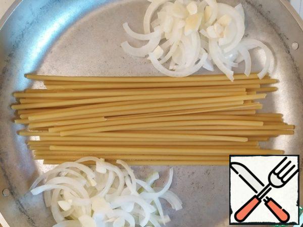 In the pan, put the spaghetti, the sides of the onion cut into half rings and finely chopped garlic.