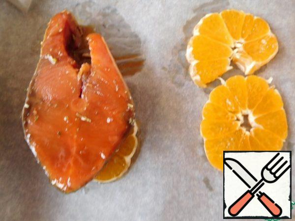 Cut the tangerine into small circles.
Place on a baking tray.
Put the fish on top and pour the remaining marinade over it.