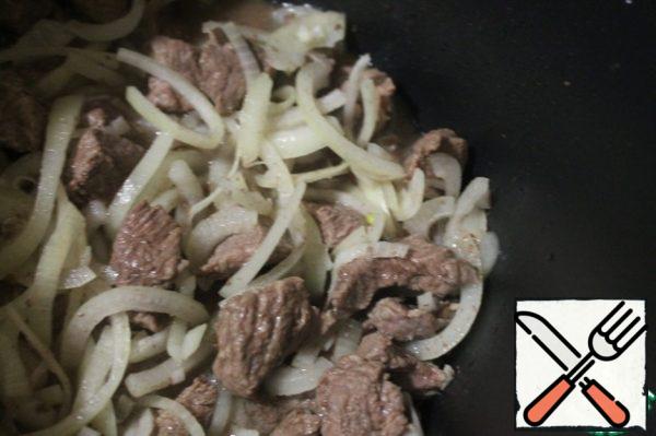 Fry the meat in a cauldron for 10 minutes, add the onion cut into half rings. Fry everything together to make the onion soft.