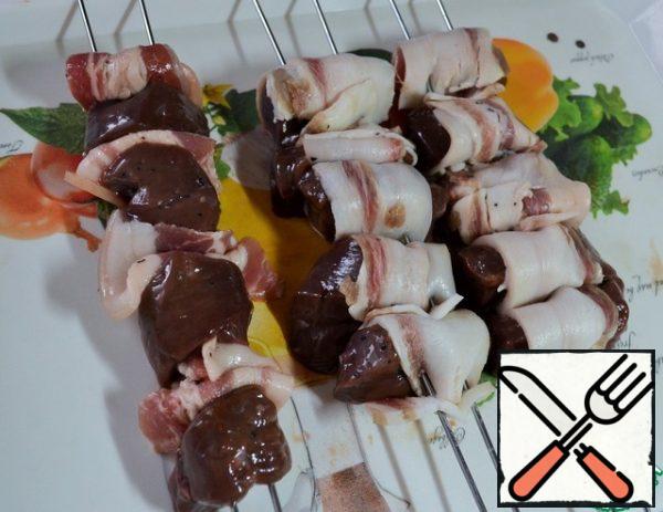 The coals on the grill are almost ready.
Sprinkle the liver with vinegar and mix.
Wrap each piece of liver in bacon and string on skewers.
It is more convenient to fry such kebabs on double skewers.

I had a force majeure - bought bacon was... to put it mildly, short and thick pieces. I strung it just alternating with the liver.
Slice the salted lard as thinly as possible, wrap the liver.
String on skewers.