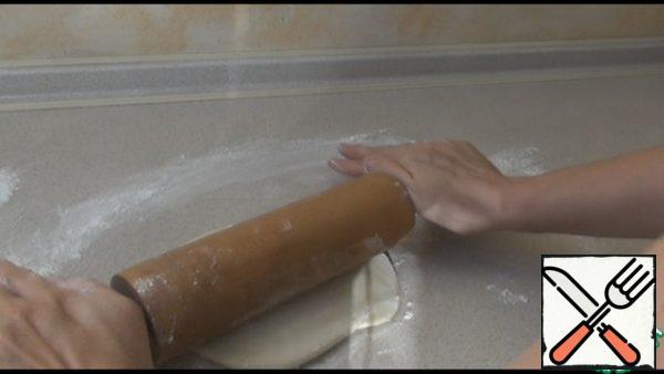 We take out the dough, divide it into two parts. One part is rolled out as thinly as possible into a rectangular layer. Dust the table with flour.