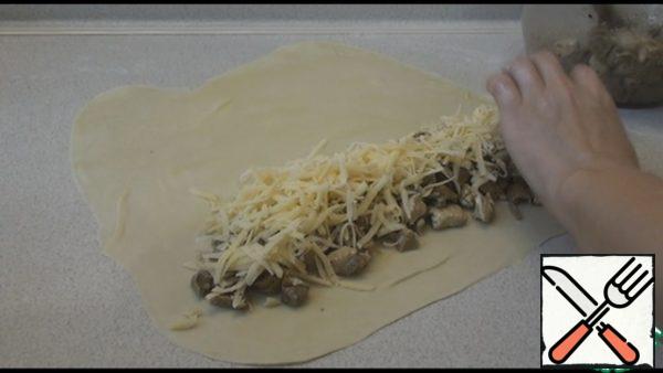 If the filling is very juicy, add 1 tbsp of starch and stir. Roll out the dough lightly smear with vegetable oil. On one side, spread half of the filling, sprinkle with half of the grated cheese.