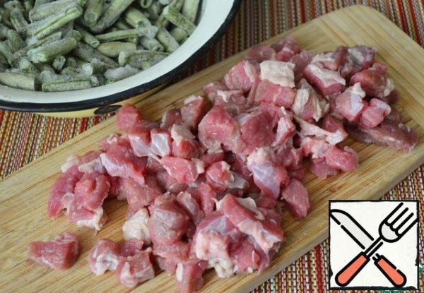 Wash the meat, dry it, and cut it into 1.5 cm pieces. . Peel the onion, cut it into feathers, and defrost the beans.