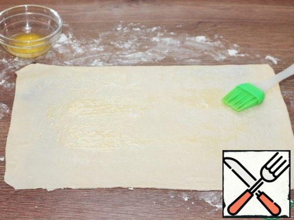 Prepare the dough. Dust the table top and rolling pin with flour. Thawed dough (1/2 part, 250 g) is rolled into a layer to the size of 27*37 cm and smeared with melted butter.