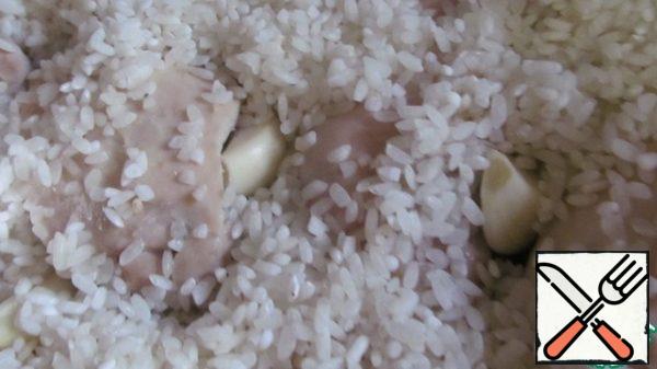 In a saucepan, heat the oil and lightly brown the chicken thigh fillet until pale yellow. If you like it, you can fry it harder.
Cover the washed raw rice. Distribute the garlic evenly, trying to place each clove in half under the fillet.