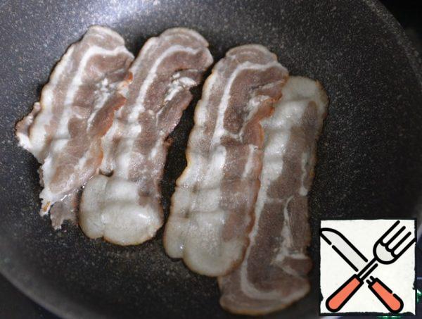 In a frying pan, fry strips of raw smoked bacon, melt the fat, remove the bacon from the pan.