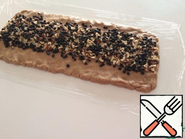 We level a 45-centimeter piece of food film on the table. We spread the dough on it and form a rectangle with our hands (as in the photo). Top with chopped nuts and chocolate pieces. Nuts can be any, I have-hazelnuts. Dark chocolate finely chopped or ready-made drops.