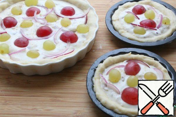 Spread the filling on the dough, on top of the onion, cut into thin half rings, put the grapes, sprinkle with nuts and, if desired, pink pepper.