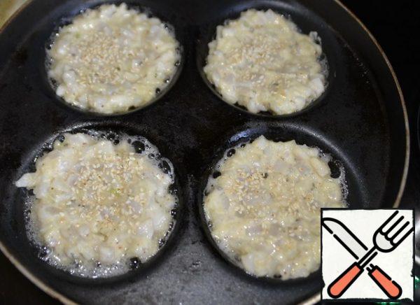 Pour the oil into a hot pan. I use a frying pan for frying pancakes. Put a full spoonful of squid "dough" on a hot frying pan with oil, lightly sprinkle sesame seeds on top. Fry on medium heat for 3 minutes.
