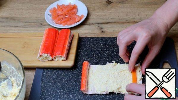 Unwrap the crab sticks and spread 1 tablespoon of the filling over the entire surface of the crab stick. Put a boiled carrot or red fish on one side. Put in the refrigerator.