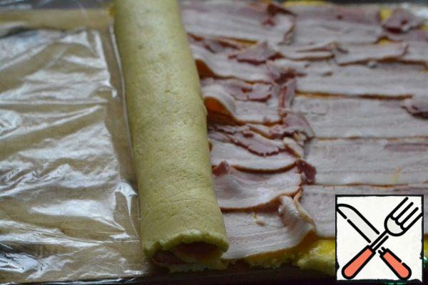 Helping yourself to the film, roll the potato dough into a roll, starting from the narrow edge.
Tighten the sides tightly and tie the ends of the film in a knot.