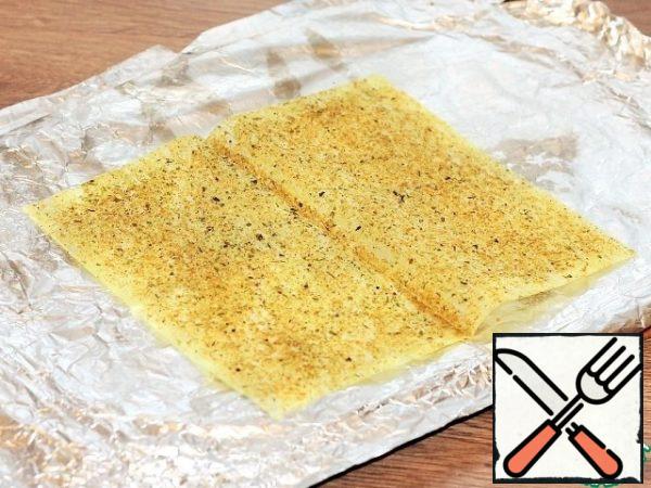 Put a piece of foil on the table top and smear the middle with sunflower oil, a little to fix the parchment. We put a piece of parchment (20 * 17 cm) on it and also lubricate it with oil. Sprinkle the parchment with ground chicken seasoning.
You can buy leaves for frying already with seasoning and cook in them.