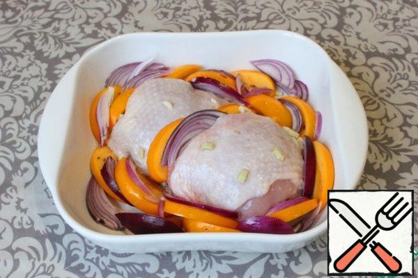 To bake the thighs in the oven, I take a small fireproof form. Spread in the center of the form of chicken thighs with pieces of garlic and ginger. Pour over the top and sides of the remaining oil in the bowl.
Around the chicken thighs I spread pieces of persimmon and red onion.