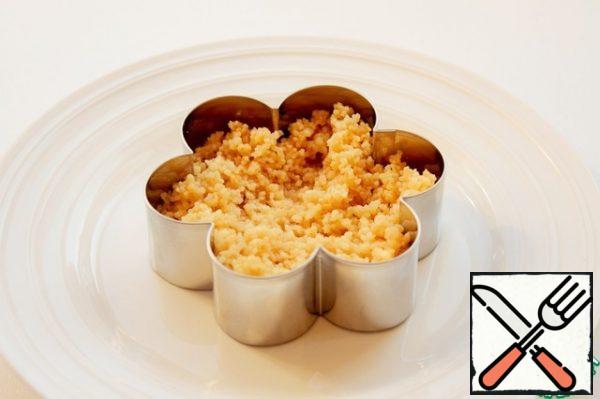 On a plate, put the serving form, I have in the form of a flower. Lay out a layer of couscous, well tamped.