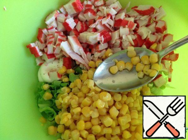 Pour in the corn. Cut the crab sticks into cubes. Mix the salad.