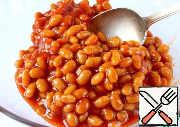 From a jar of spicy canned chili beans, we will pour some of the liquid into a separate container and set aside, it will still be useful to us.
Beans with the remaining liquid are transferred to a salad bowl.