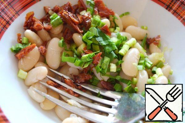 Finely chop the sun-dried tomatoes, add them to the beans, and add the cherries here. Lightly chop the beans with a fork. Crush about half the beans. Why is this necessary? The dressing will penetrate the mashed beans, soak them, and the salad will be much juicier.