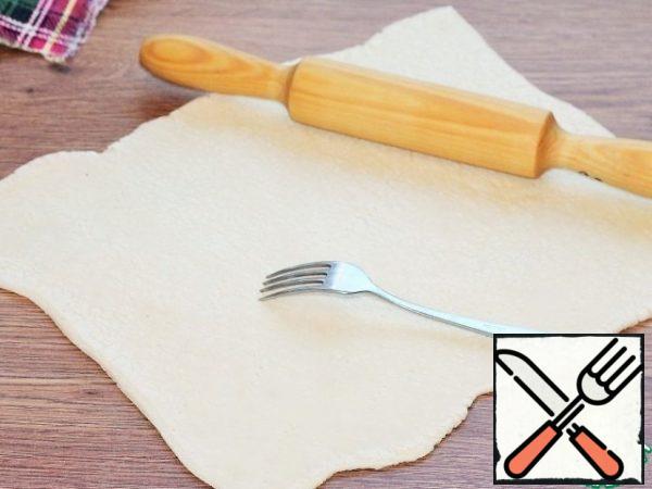A plate of puff pastry is placed on a table top dusted with flour and rolled out 1.5 times. Pierce the dough with a fork.
