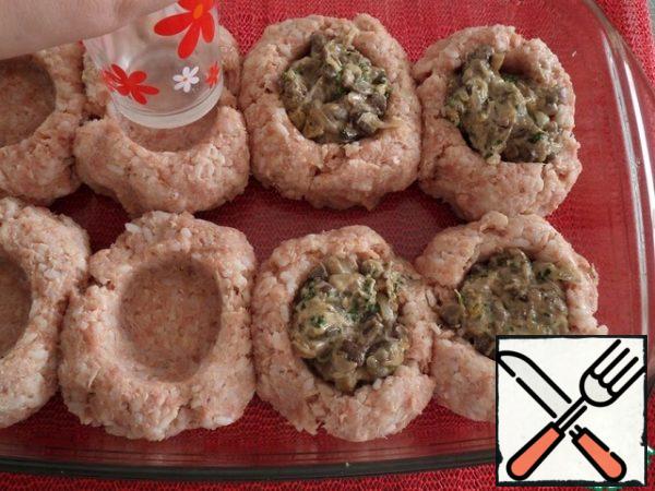 Then, using a glass moistened with water, we make depressions in each meat ball. In the resulting recesses, we spread the prepared mushroom filling.