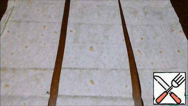 Let's make pita bread. My package consists of 3 sheets each of 100 g. I cut each of them into 3 strips about 12X45 cm in size. There were 9 stripes in total.