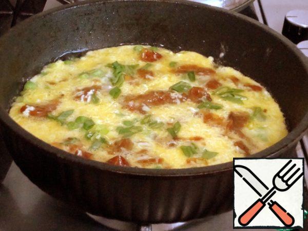In a frying pan, pour vegetable oil and lightly fry the onion with green peas.
Then pour in the egg mixture, cover and cook over low heat. 2 minutes before cooking, add the greens..
I did not salt the omelet - we had enough salt from cheese and tomatoes.