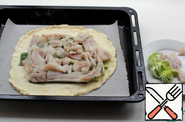 Take the dough out of the refrigerator and divide it into 2 parts. Roll out one part, put it on parchment and on a baking sheet, put the leek sheets on top of the fish fillet on the dough, add salt.