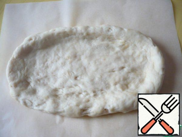 Transfer the dough to the prepared sheet of parchment paper and form an oval of dough even thinner with your fingers. Do the same with the rest of the dough pieces. Leave the pizza bases for 10 minutes, covering them with cling film.