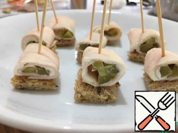 To form a canape, first put a piece of bread, spread a ham roll on top and pierce with a skewer. So we repeat with all the canapes.