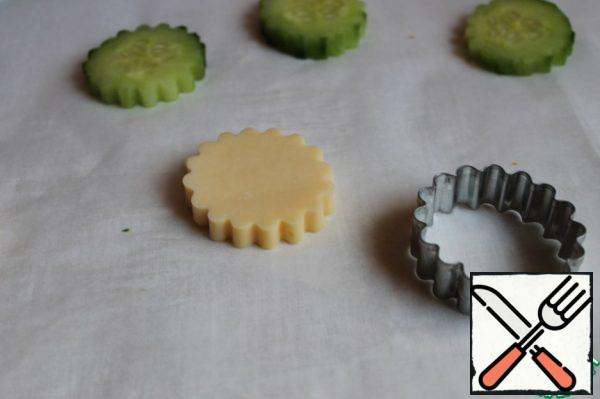 We cut the cucumber into washers. Cheese is also cut into a thickness of about 0.5 cm. And we squeeze out such flowers with a mold. If there is no form, you can do it with a shot glass.