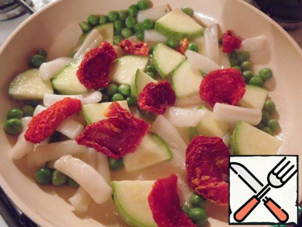 To the squid, add the zucchini, peas and dried tomatoes, cut into quarters, and fry for 3-4 minutes.