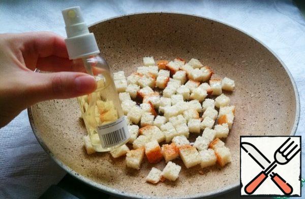 Next, we transfer the bread cubes to the pan, lay them in an even layer and sprinkle with oil from such a bottle with a spray bottle. The advantage of this method is that the bread will not float in the oil, but each cube will be well and evenly soaked, with less oil consumption. The jar can be purchased at any cosmetics or household goods store.