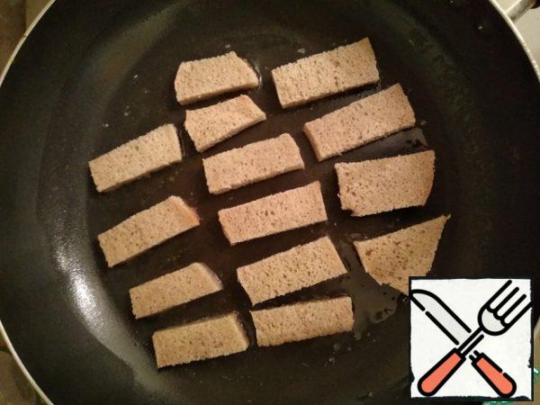 My bread turned out to be gray, although this is not essential. But I prefer croutons made of black and gray bread. Trim the edges, in the photo I already did it. Also prepare vegetable oil, garlic and cheese . In a frying pan on hot oil, fry the garlic for a couple of minutes and take it out. In garlic butter, we send bread.