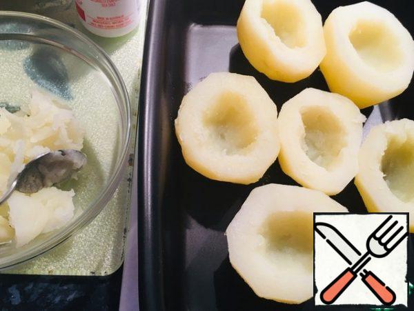 Potatoes should preferably be of the same size, peeled and boiled almost to readiness :potatoes should not be overcooked. I cut the potatoes into two parts, dry, cut off the tops so that the potatoes can be put on a baking sheet.
On the other side of the potato, cut out the middle or take out the potatoes with a teaspoon in another bowl.