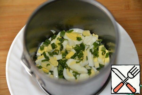 On a plate (dish) put the cooking ring (split form), put the bottom layer of eggs with green onions, lightly tamp.