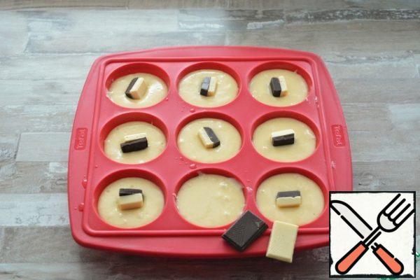 Spread the dough on the muffin molds. In the middle of each cake, place a piece of dark and white chocolate.

Place in a cold (!) oven. Turn on 150-160°C and bake until the cupcakes rise. Then increase the temperature to 180°C and bake the cupcakes until ready. Check with a toothpick. I baked for about 20 minutes. Be guided by your oven.