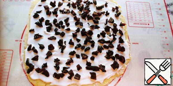 Then we take out and roll it out not very thinly, by 5-7 millimeters, preferably on a rug or paper.
Beat one protein with sugar, I have 2 spoons, and grease the dough. Sprinkle with chopped prunes and roll into a roll, helping yourself with a rug.