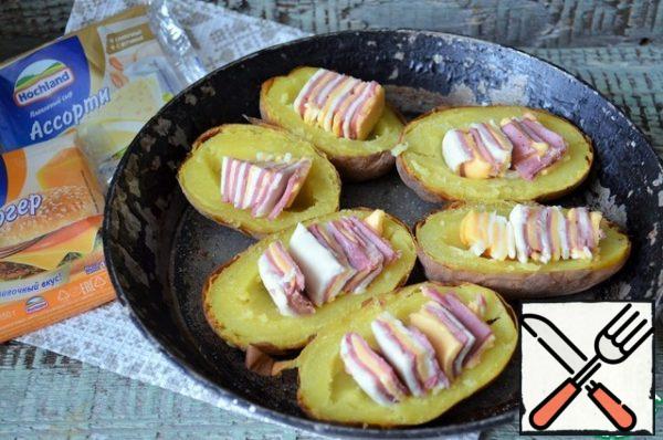 Remove part of the pulp from the potatoes, press down, making blanks, add salt. Spread the cheese and ham in the potatoes, sprinkle with paprika.