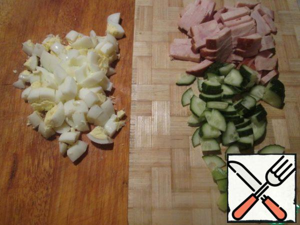 Boil the eggs, peel and cut them. Cut the cucumber and avocado into cubes, and the ham into strips.