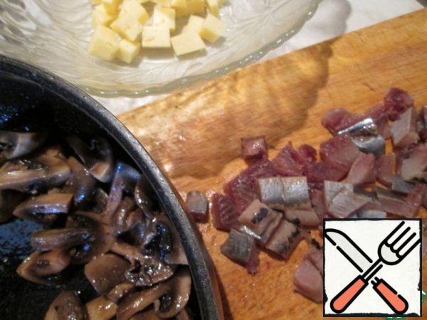 Cut the herring into small pieces, cut the cheese into cubes, and fry the quarters of the mushrooms in butter.