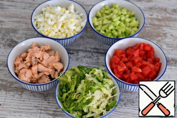 Salad can be prepared with almost any fish. Mackerel, salmon, tuna, cod. Even with the usual pollock, this salad is very good. The fish can be boiled, baked, or hot-smoked. This time I was preparing a salad with baked pink salmon.
Separate the fish into segments.
Peel the cucumbers (two small ones) and cut them into small cubes.
Cut a large tomato into cubes of the same size. Use only the pulp, seeds and juice to remove.
Chop the boiled eggs.
Chop the Peking cabbage into thin strips.