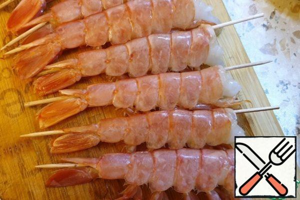 Remove the heads of the shrimps. Pass the skewer through the shrimp in the area of the esophagus. This is necessary so that the shrimp remains straight during cooking.