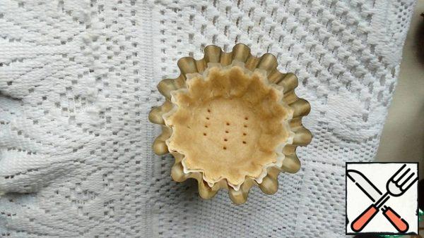 Divide the dough into pieces and form baskets, evenly distributing them over the tins. We press well at the junction of the bottom with the side wall. We prick the bottom with a fork so that it does not swell when baking.