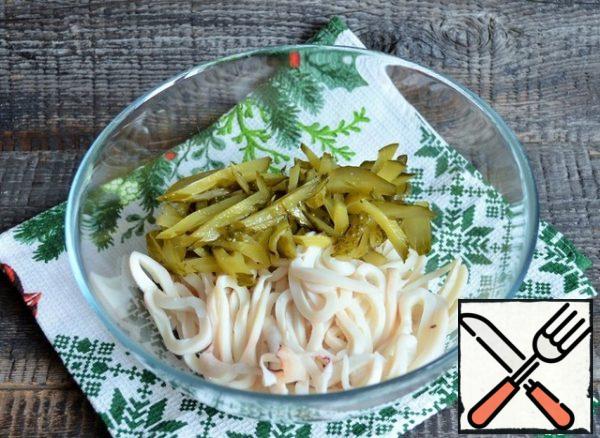 Cut the squid and pickled cucumbers into thin strips and put them in a salad bowl.