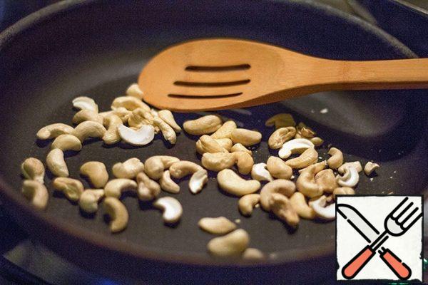 Fry the cashew nuts in a dry pan, stirring, until they have a characteristic smell and golden color, about 3 minutes.
