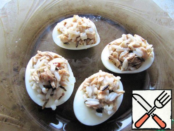Hard-boiled chicken eggs, peeled, cut into 2 halves. Remove the yolk and use it in another dish. Fill the egg halves with rice and fish preparation, sprinkle with herbs and garnish with olives. Cut the bread into serving pieces, put the stuffed egg on it.