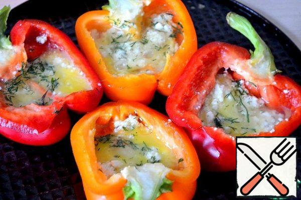 In the peppers, put the crushed cheese with herbs.
If the eggs are small , put 1 egg in each half. If large, break into a bowl, stir and distribute equally among the peppers.