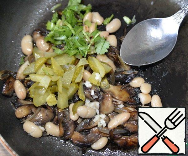 With the beans, we drain the liquid, put it to the mushrooms. Add the chopped pickled cucumber, squeeze out the garlic, put the chopped coriander greens, mix.