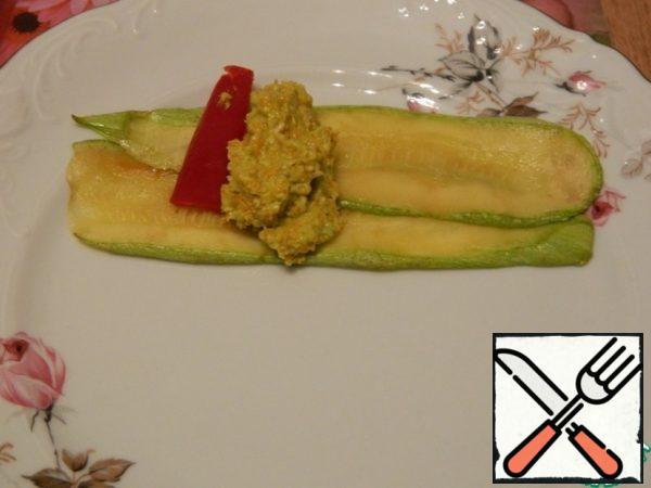 We put two strips of zucchini on a plate, put the filling, a strip of pepper on it and cook it with a roll.